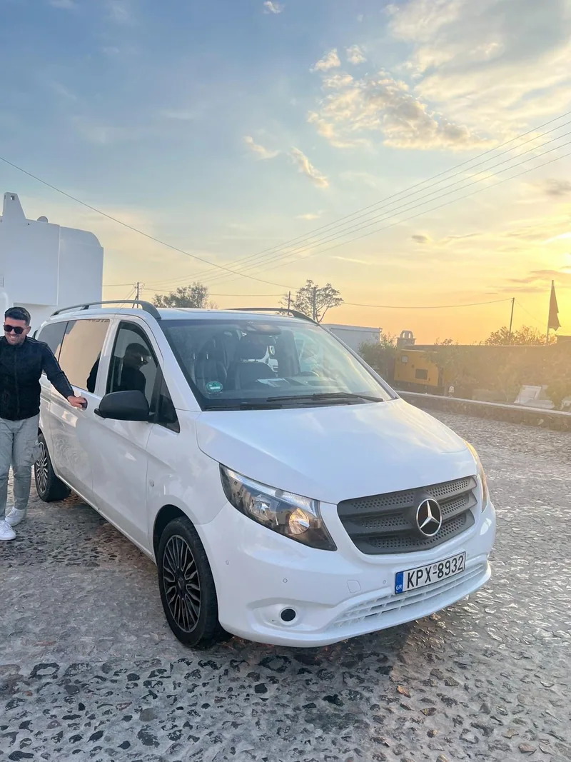 Vangelis standing beside his white Mercedes Vito at sunset in Santorini